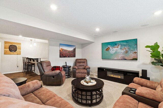 living room featuring a glass covered fireplace, wood finished floors, recessed lighting, and baseboards