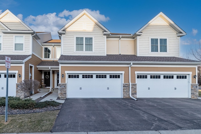 townhome / multi-family property with an attached garage, stone siding, and aphalt driveway
