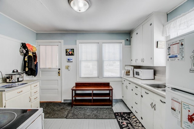 329 Main St NW, Menahga, MN 56464 - kitchen with white appliances, white cabinetry, light countertops, a sink, and crown molding