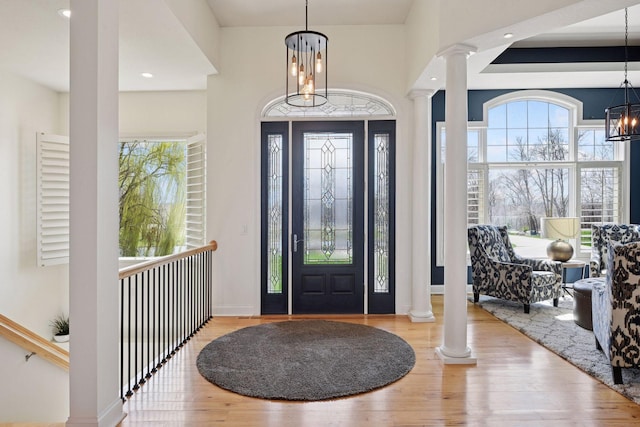 foyer with a healthy amount of sunlight, decorative columns, wood finished floors, and an inviting chandelier