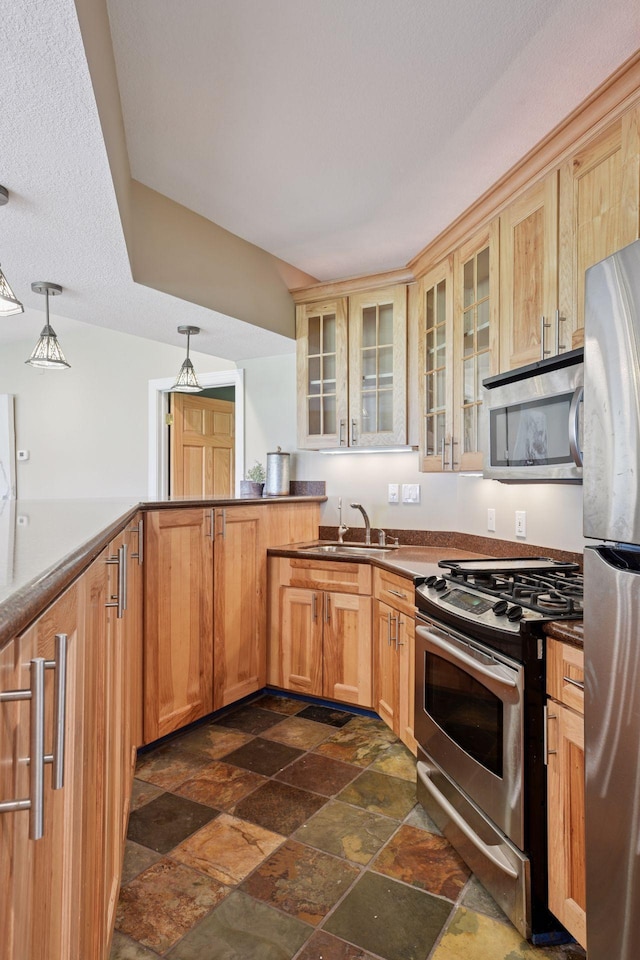 kitchen with glass insert cabinets, a sink, appliances with stainless steel finishes, stone tile flooring, and dark countertops