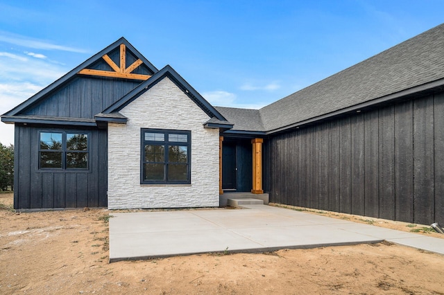 view of front of house featuring board and batten siding, a patio, a shingled roof, and stone siding