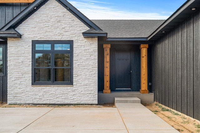 entrance to property with a shingled roof and stone siding