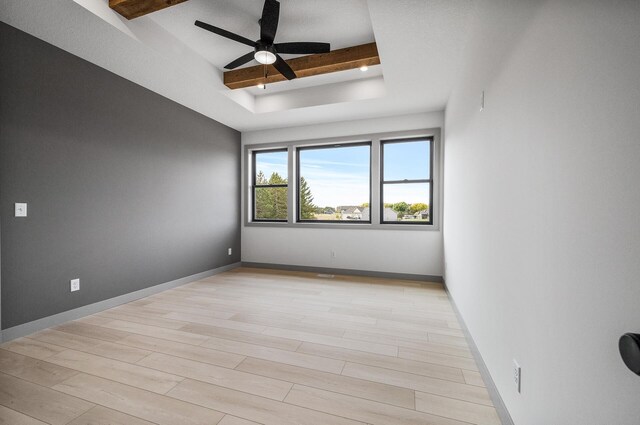 spare room with ceiling fan, beam ceiling, a raised ceiling, and light wood-style floors