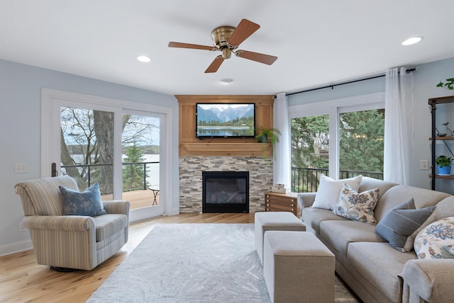 living area featuring ceiling fan, a stone fireplace, recessed lighting, and light wood-style flooring