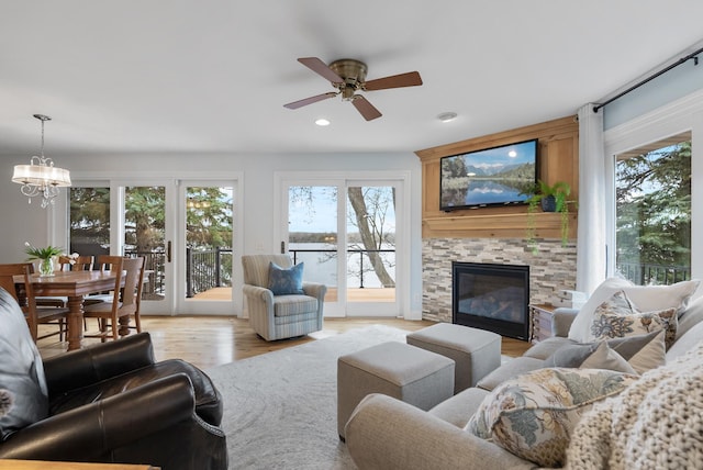 living room with recessed lighting, a stone fireplace, ceiling fan with notable chandelier, and light wood-type flooring