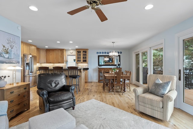 living room featuring baseboards, light wood-type flooring, ceiling fan with notable chandelier, and recessed lighting