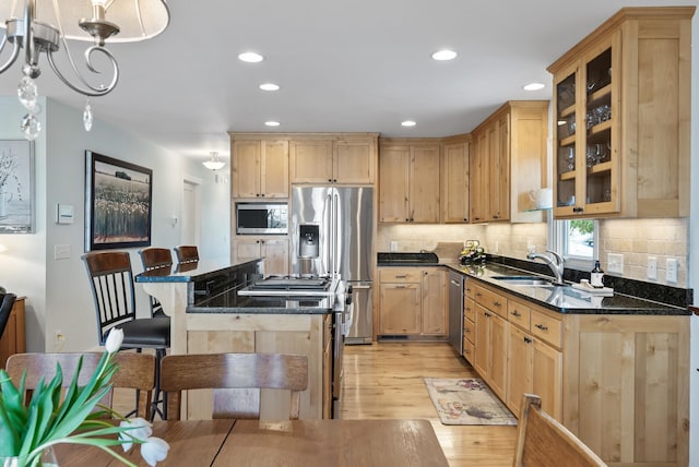 kitchen with appliances with stainless steel finishes, a sink, light wood finished floors, and light brown cabinets