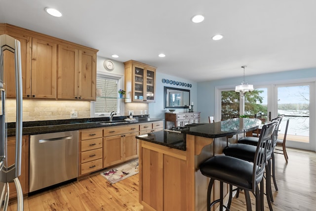 kitchen featuring stainless steel dishwasher, a breakfast bar area, a center island, light wood-style flooring, and backsplash