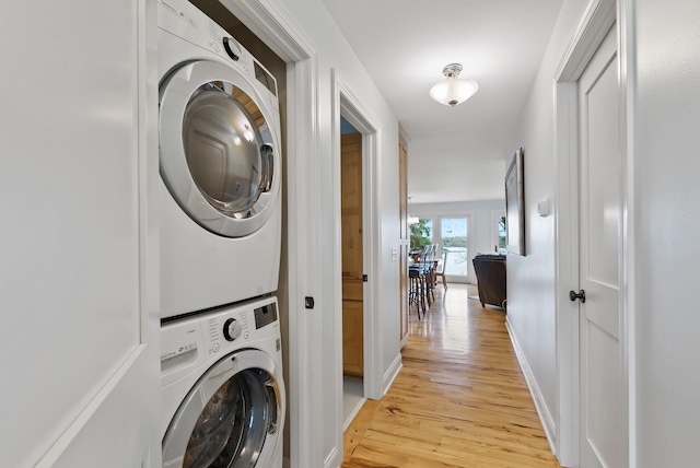 laundry area featuring baseboards, laundry area, light wood-style flooring, and stacked washer / dryer