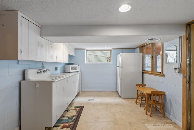 kitchen featuring white cabinets, a sink, white appliances, concrete block wall, and visible vents