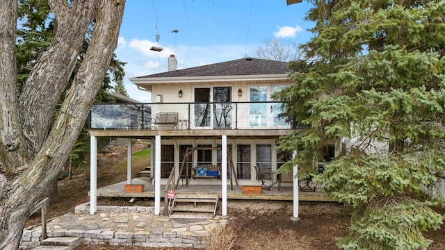 rear view of property featuring roof with shingles, a wooden deck, a chimney, and a balcony