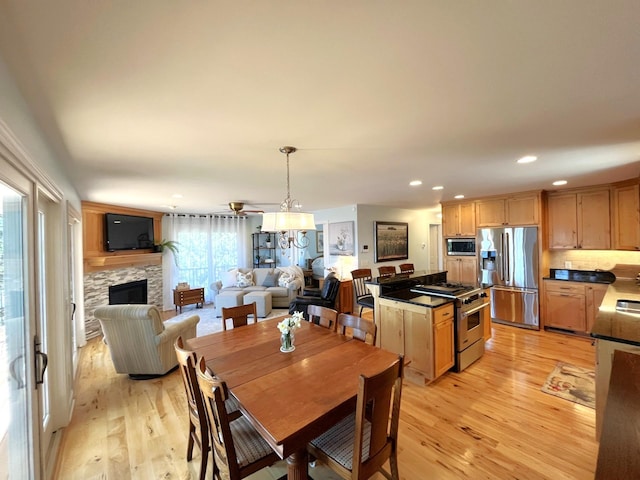 dining area with recessed lighting, a ceiling fan, a stone fireplace, and light wood-style floors