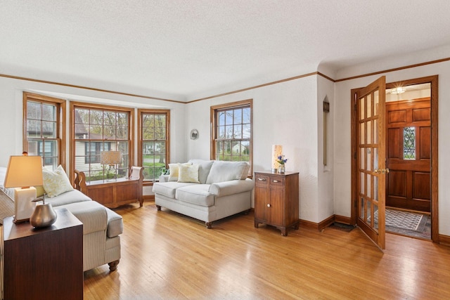 living room with light wood-style floors, baseboards, ornamental molding, and a textured ceiling