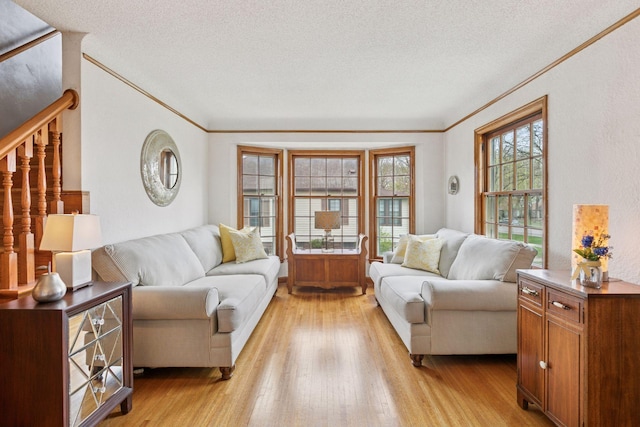 living room featuring crown molding, a textured ceiling, light wood-style flooring, and stairs