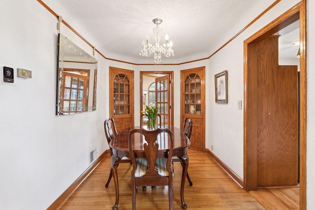 dining space with a textured ceiling, light wood-type flooring, visible vents, a chandelier, and baseboards