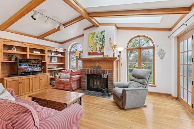 living area featuring vaulted ceiling with skylight, track lighting, a fireplace, light wood-style flooring, and baseboards