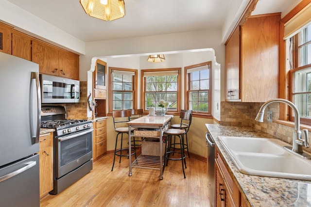 kitchen featuring light wood finished floors, a sink, stainless steel appliances, brown cabinetry, and decorative backsplash