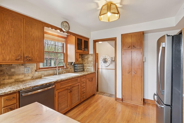 kitchen featuring light wood finished floors, brown cabinets, a sink, stainless steel appliances, and backsplash