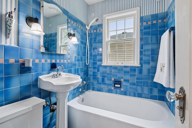 full bath featuring wallpapered walls, toilet, tile walls, and shower / bath combination