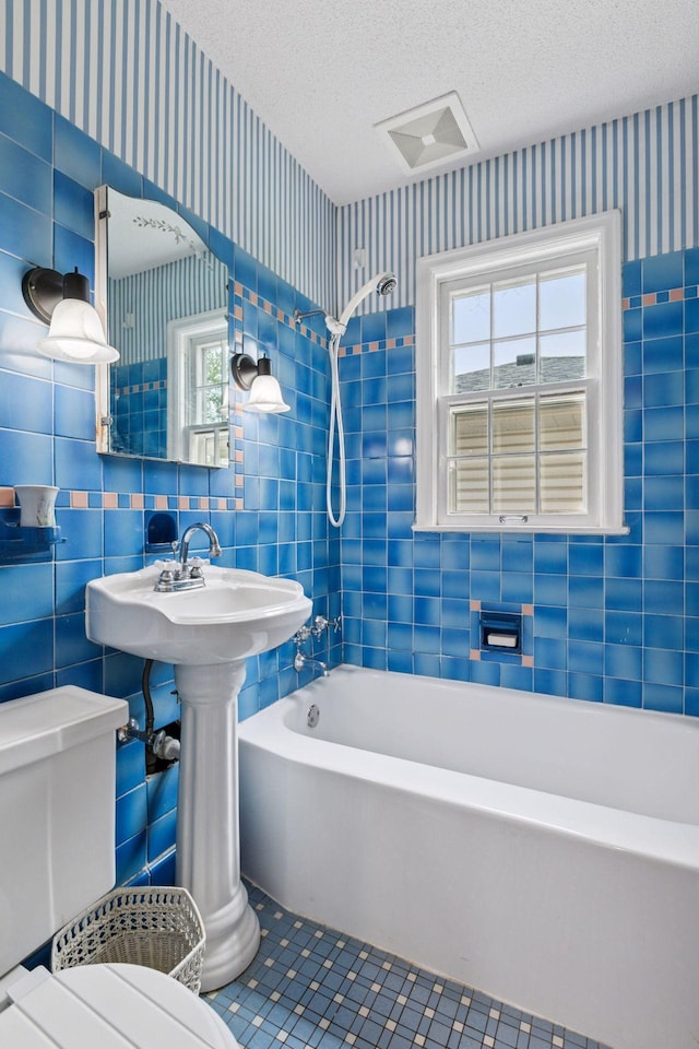full bathroom with wallpapered walls, toilet, and tile walls