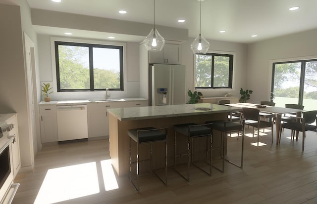 kitchen featuring stainless steel fridge with ice dispenser, a kitchen island, a sink, a wealth of natural light, and white dishwasher
