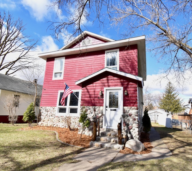 view of front facade featuring stone siding, fence, and a front lawn