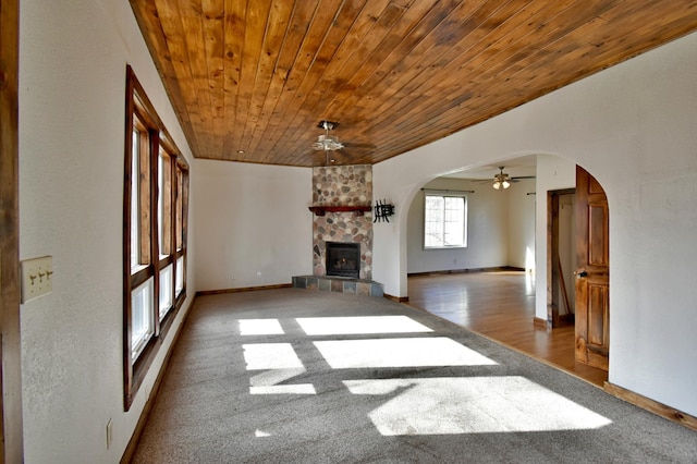 unfurnished living room with baseboards, a fireplace, ceiling fan, arched walkways, and wooden ceiling