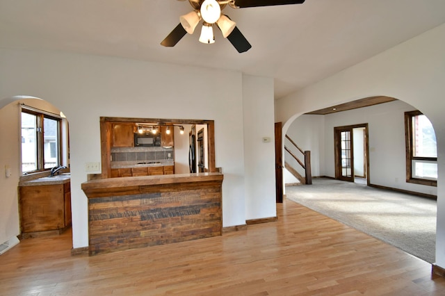 unfurnished living room featuring ceiling fan, light wood finished floors, arched walkways, and stairway