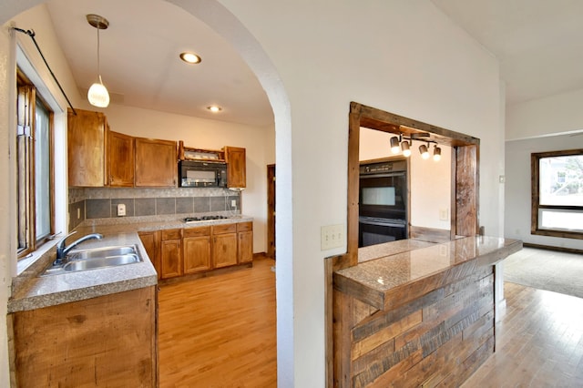 kitchen featuring a sink, light wood-type flooring, black appliances, and arched walkways