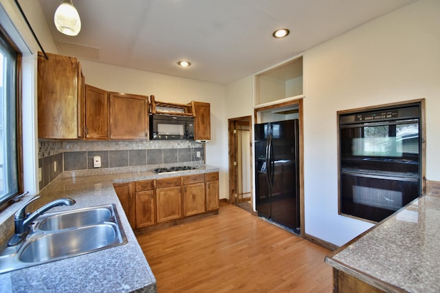 kitchen featuring backsplash, black appliances, light wood-style floors, brown cabinetry, and a sink