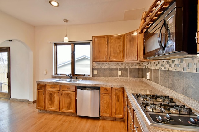 kitchen featuring stainless steel appliances, light wood finished floors, brown cabinets, and a sink