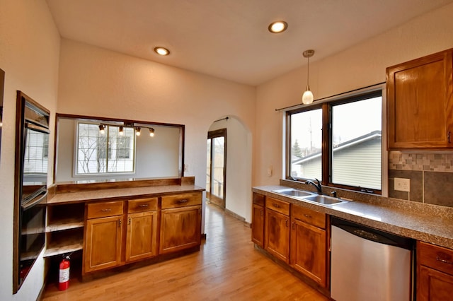 kitchen featuring stainless steel dishwasher, brown cabinetry, a sink, and a healthy amount of sunlight