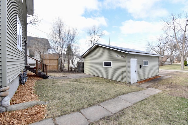 view of side of home with an outdoor structure, fence, and a lawn