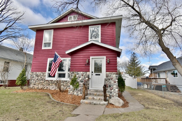 traditional style home with a front yard, stone siding, and fence
