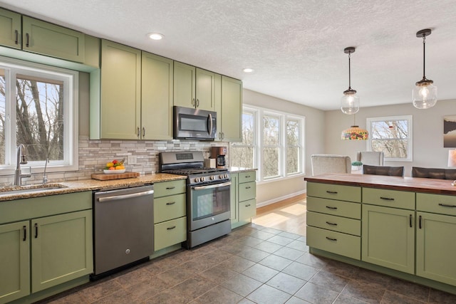 kitchen with pendant lighting, green cabinets, appliances with stainless steel finishes, a sink, and backsplash