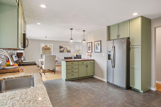 kitchen with baseboards, appliances with stainless steel finishes, green cabinetry, pendant lighting, and a sink