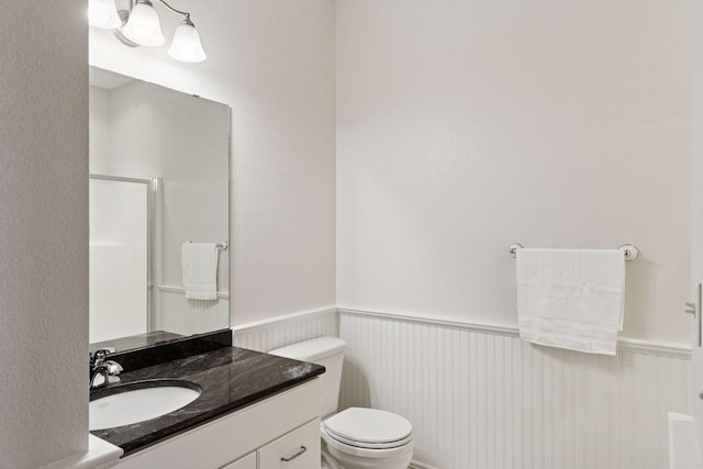bathroom with a shower, a wainscoted wall, vanity, and toilet