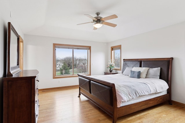 bedroom featuring light wood-type flooring, a ceiling fan, baseboards, and multiple windows