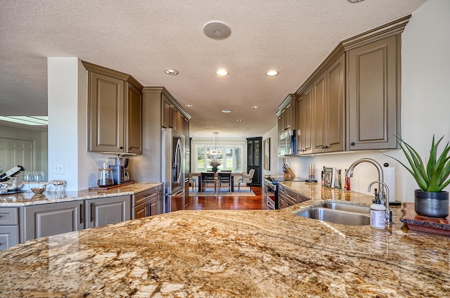 kitchen with light stone countertops, recessed lighting, a textured ceiling, a sink, and appliances with stainless steel finishes