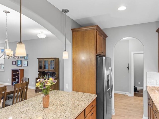 1128 Willowbrook Cir, Delano, MN 55328 - kitchen featuring stainless steel fridge with ice dispenser, arched walkways, brown cabinetry, light wood finished floors, and light stone countertops