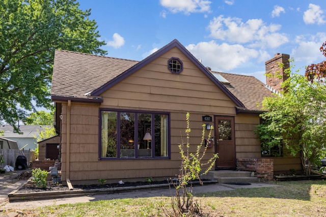 view of front facade with a chimney, a shingled roof, and fence