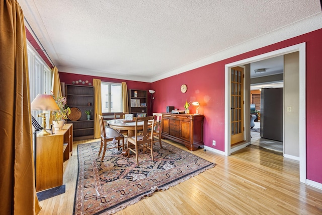 dining area featuring light wood-type flooring, a textured ceiling, and baseboards