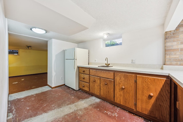 kitchen featuring freestanding refrigerator, brown cabinets, a sink, light countertops, and a textured ceiling