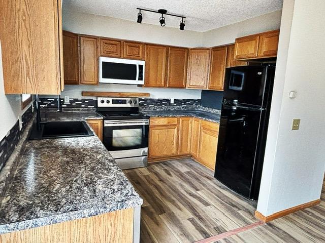 kitchen featuring wood finished floors, stainless steel range with electric stovetop, a sink, white microwave, and freestanding refrigerator