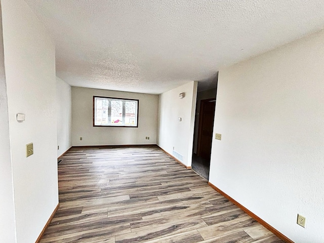 empty room with baseboards, a textured ceiling, and wood finished floors