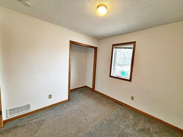 empty room featuring visible vents, a textured ceiling, carpet, and baseboards