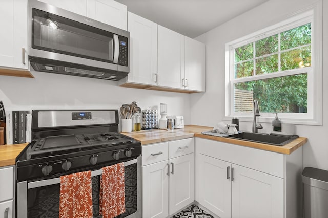 kitchen with a sink, stainless steel microwave, white cabinets, butcher block counters, and gas range
