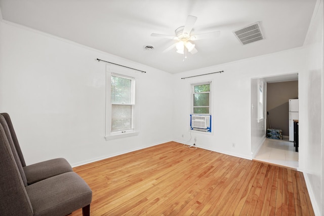 living area with a wealth of natural light, visible vents, light wood-style flooring, and ceiling fan