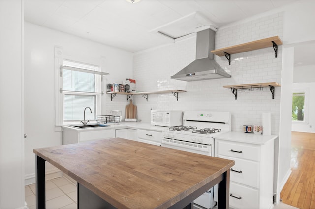 kitchen with white appliances, open shelves, a sink, wall chimney range hood, and a wealth of natural light